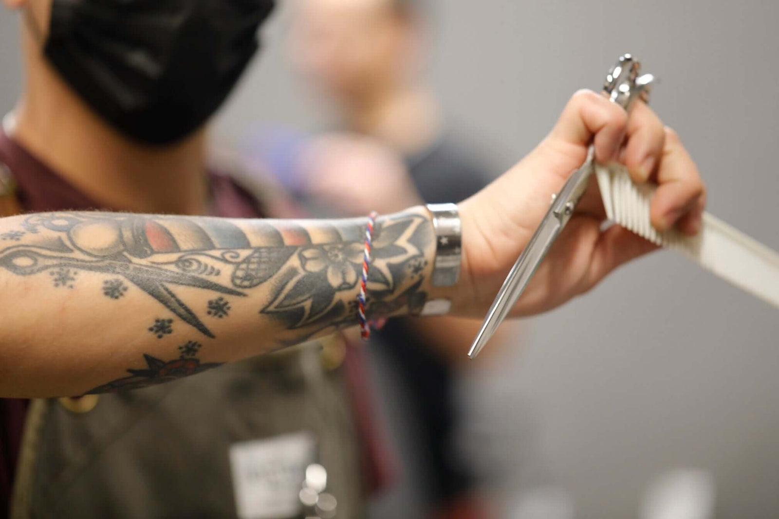Barber holding convex edge shears and comb during a haircut, showcasing tattooed forearm and precision grip.