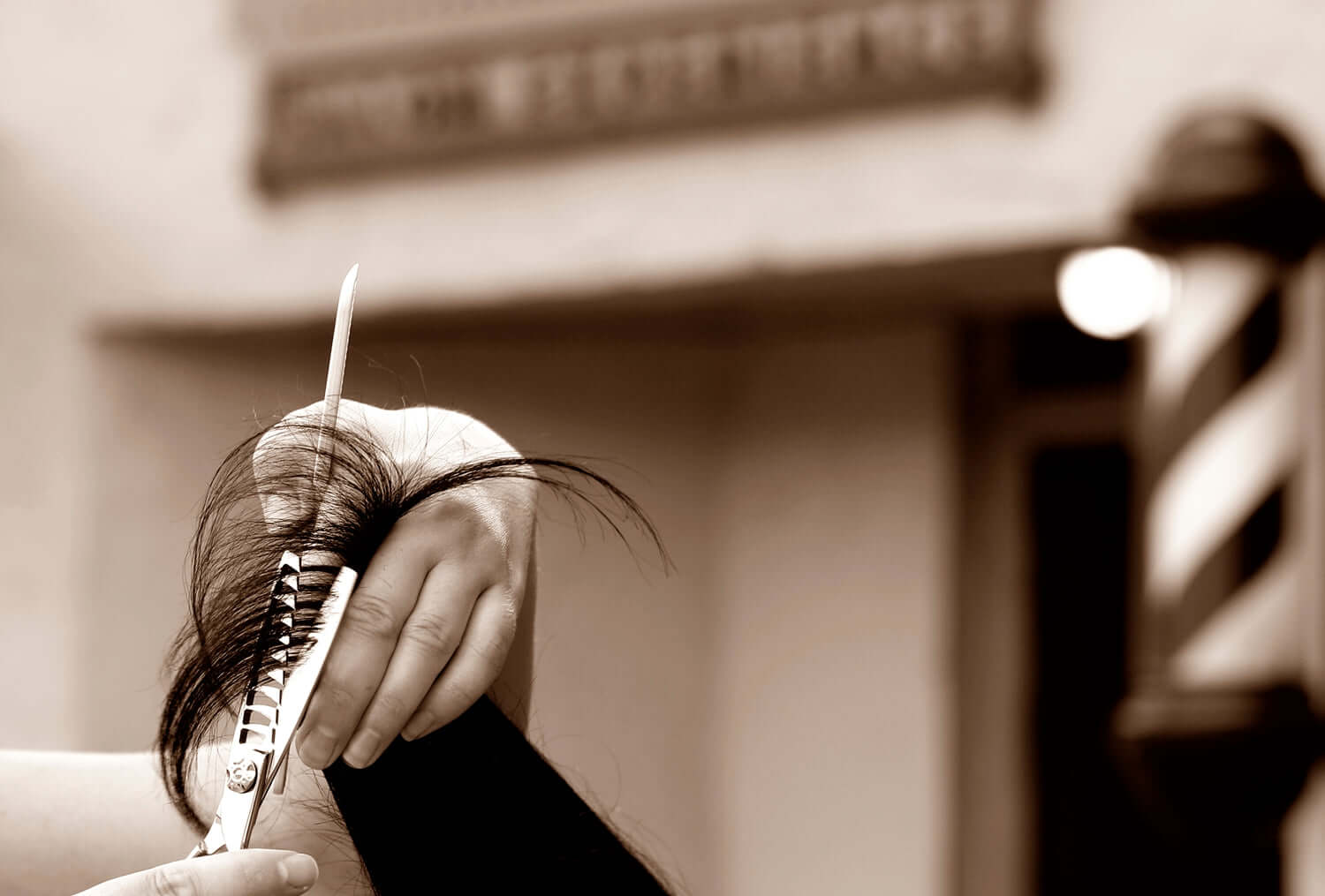 Barber using thinning shears to texturize hair outside a barbershop with a classic barber pole in the background