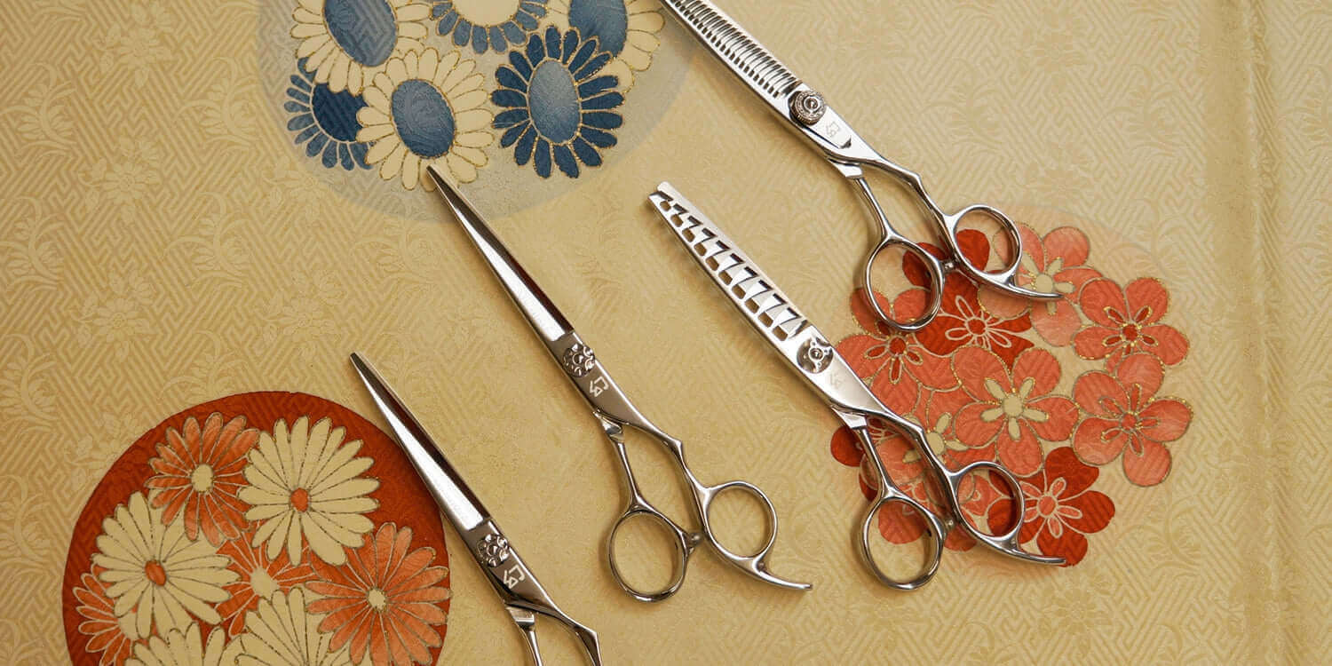 A set of professional hairdressing scissors, including straight cutting, thinning, and texturizing scissors, displayed on a decorative floral background.