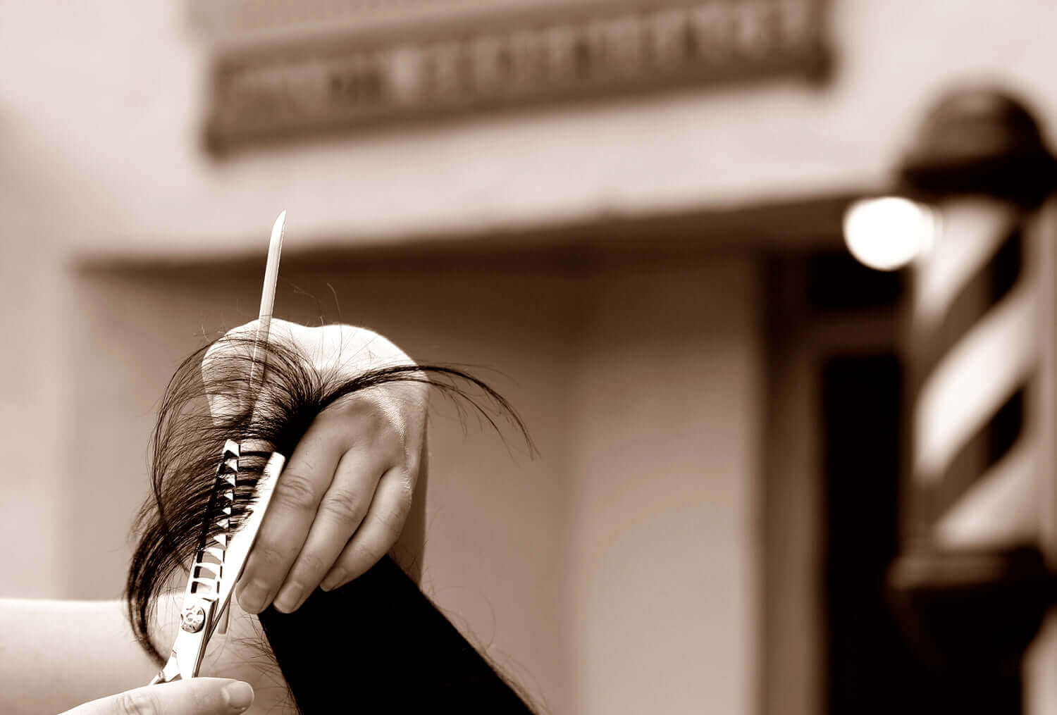 Barber using thinning shears to texturize hair outside a barbershop with a classic barber pole in the background