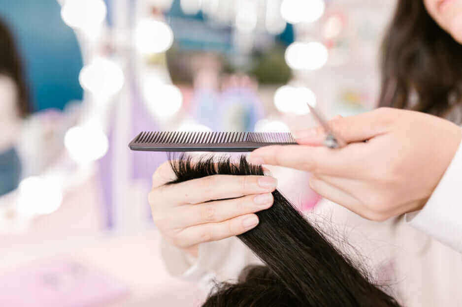 Hairdresser trimming black hair with salon scissors and comb, showcasing professional haircut technique in modern beauty salon setting.