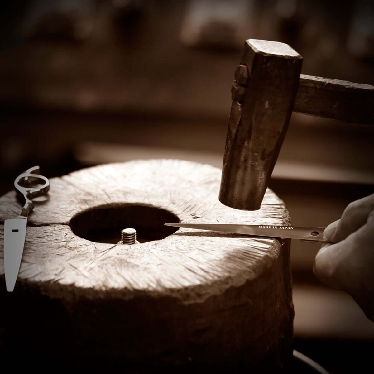 Depicting the hammering of a scissor blade, an essential step in the hair scissor sharpening process.