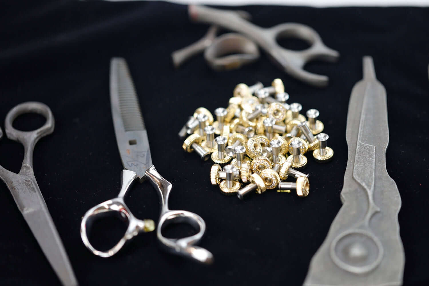 Hairdressing scissors, parts, and handles displayed on a black cloth during the scissor manufacturing or assembly process.