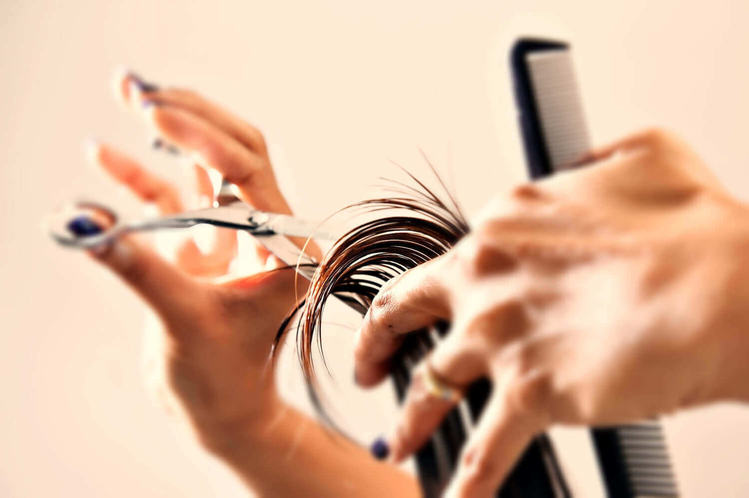 Close-up of professional hairstylist cutting hair with precision scissors and comb, showcasing salon haircutting technique and tool control.