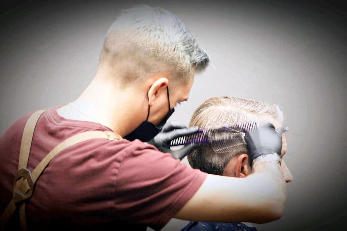 A barber performs scissor-over-comb technique on customer's hair. 