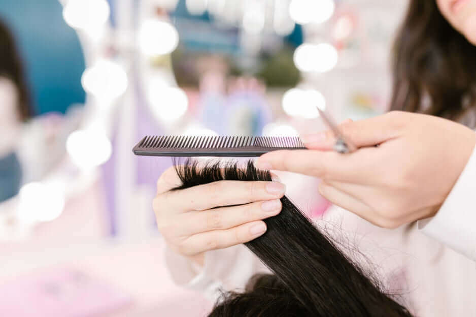 Hairdresser trimming black hair with salon scissors and comb, showcasing professional haircut technique in modern beauty salon setting.