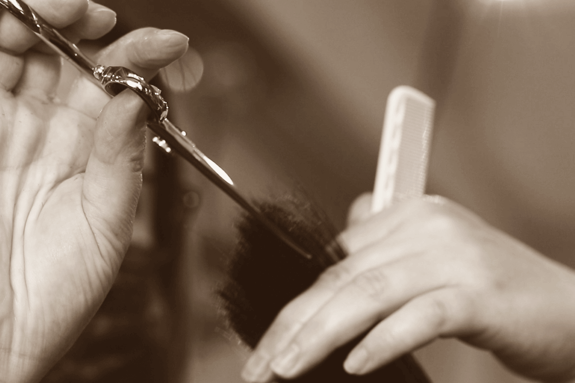 Close-up of a hairstylist’s hands using professional scissors to trim wet hair, with a comb in the background and focus on precise layering technique.