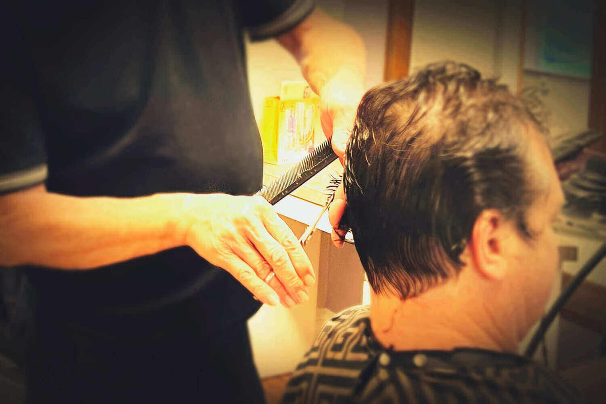 A hair stylists cuts a men's hair using hair cutting scissors.