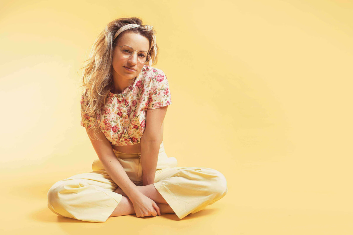 Woman sitting on the floor wearing a floral blouse and yellow pants, showcasing hair styling and beauty in salons.