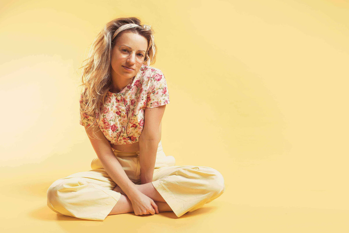 Woman sitting on the floor wearing a floral blouse and yellow pants, showcasing hair styling and beauty in salons.