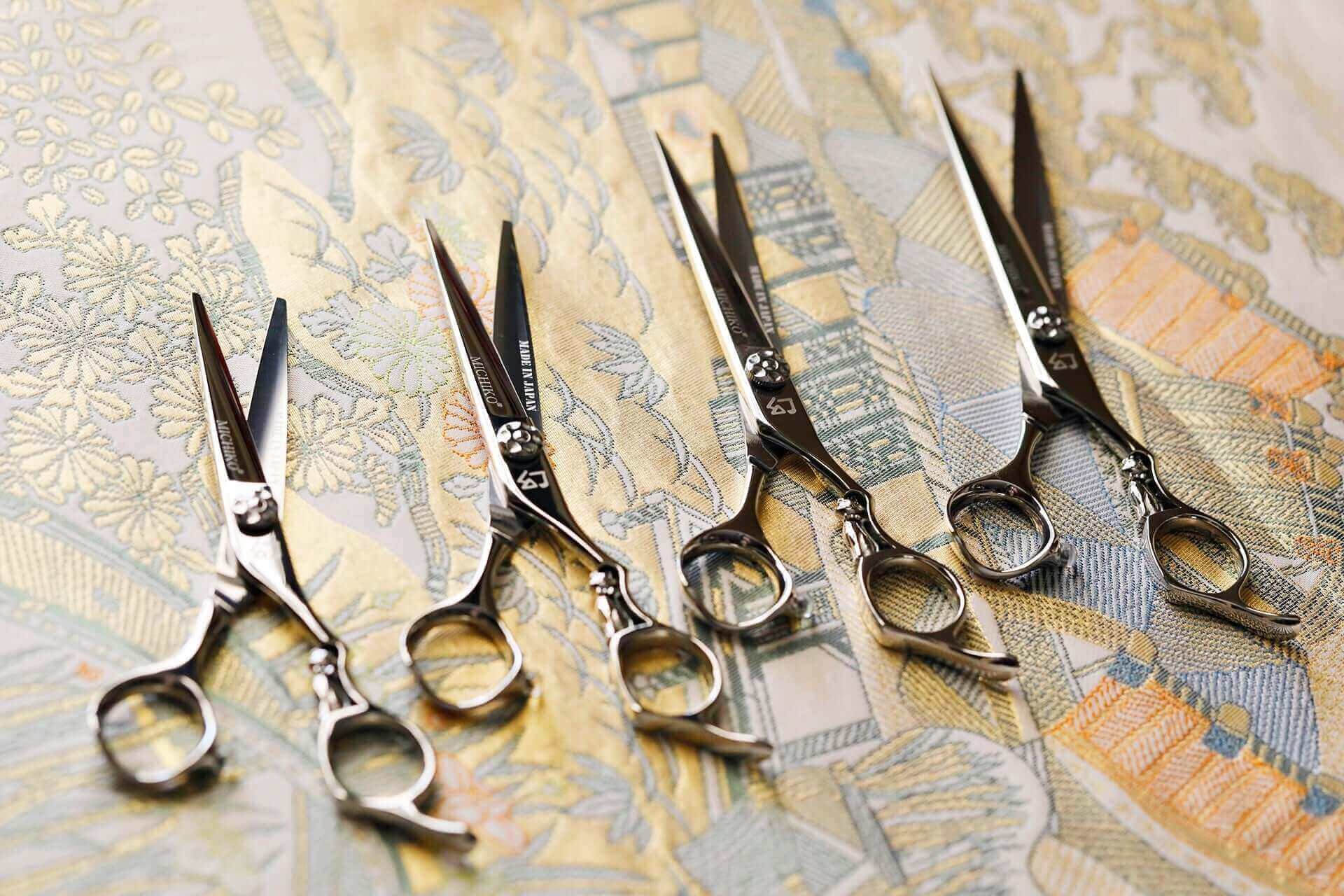 Various sizes of hair cutting scissors displayed in an open position against an oriental-themed background.