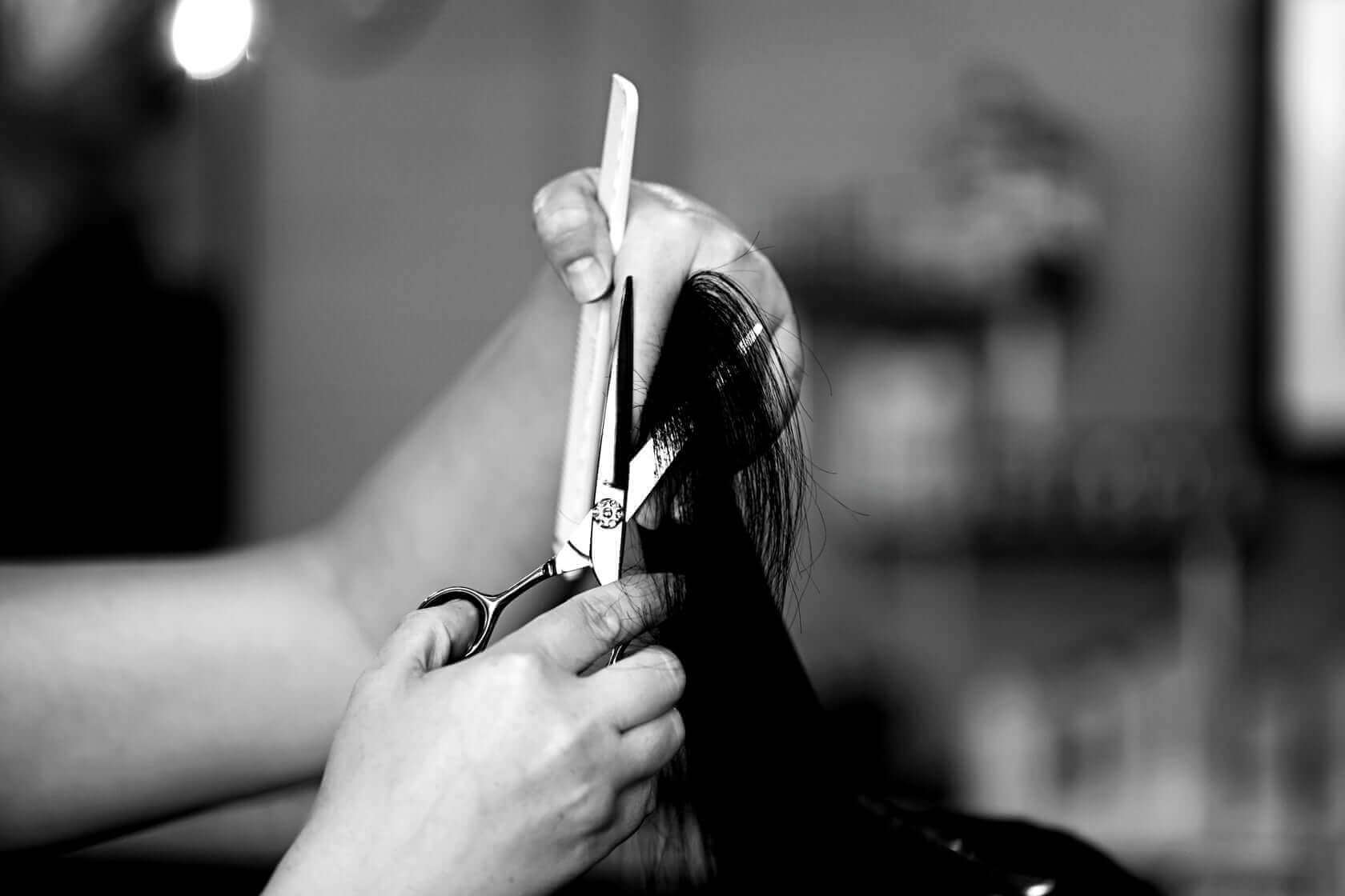 Black and white close-up of a hairstylist expertly cutting hair with professional scissors and a comb in a salon.