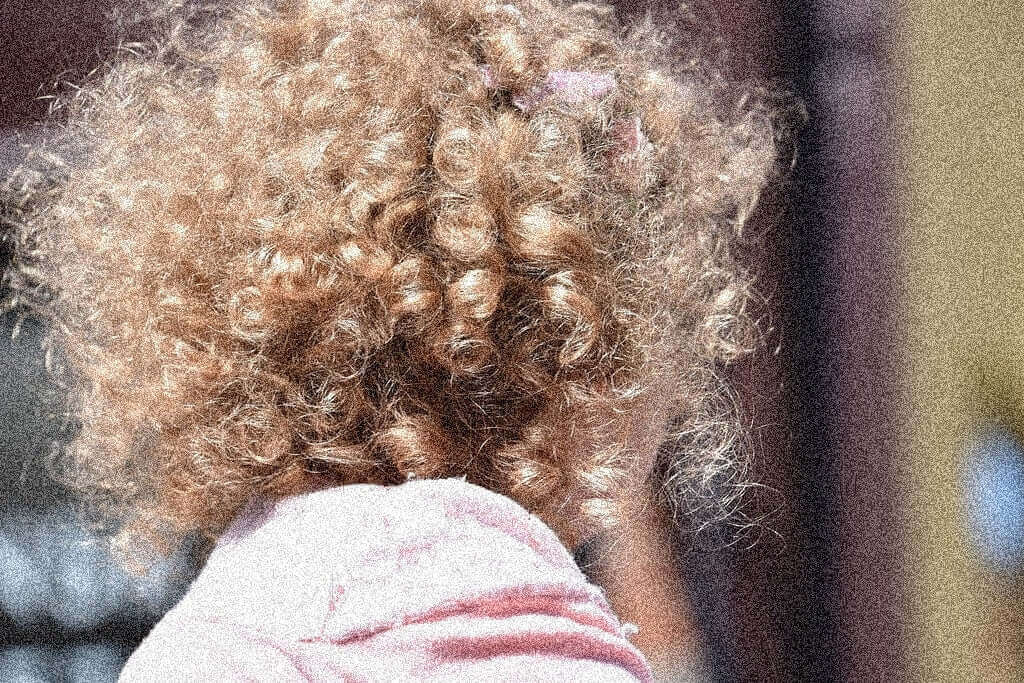 Child with natural blonde curly hair, showcasing tight curls and textured volume outdoors, ideal for blogs about cutting and styling curly hair.