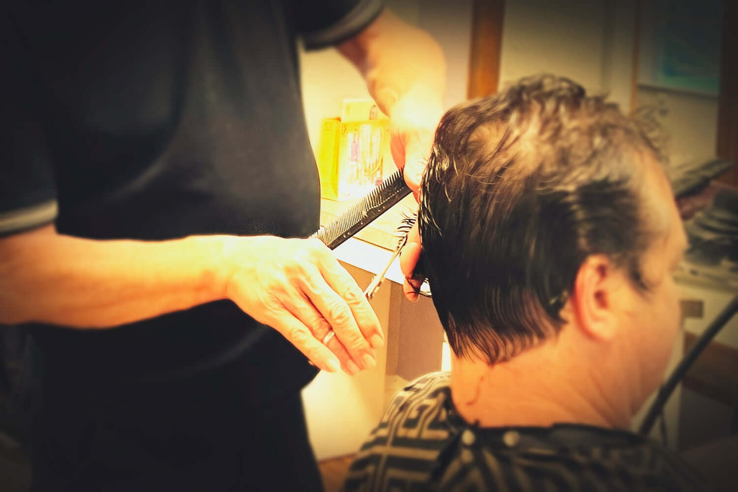 A hair stylists cuts a men's hair using hair cutting scissors.