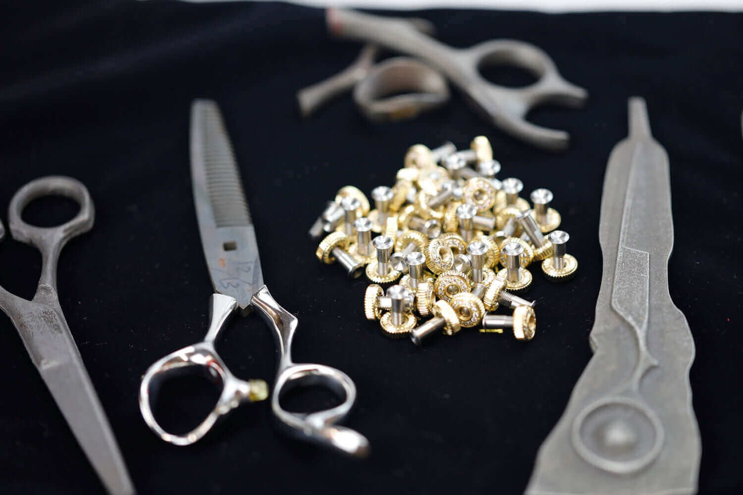 Hairdressing scissors, parts, and handles displayed on a black cloth during the scissor manufacturing or assembly process.