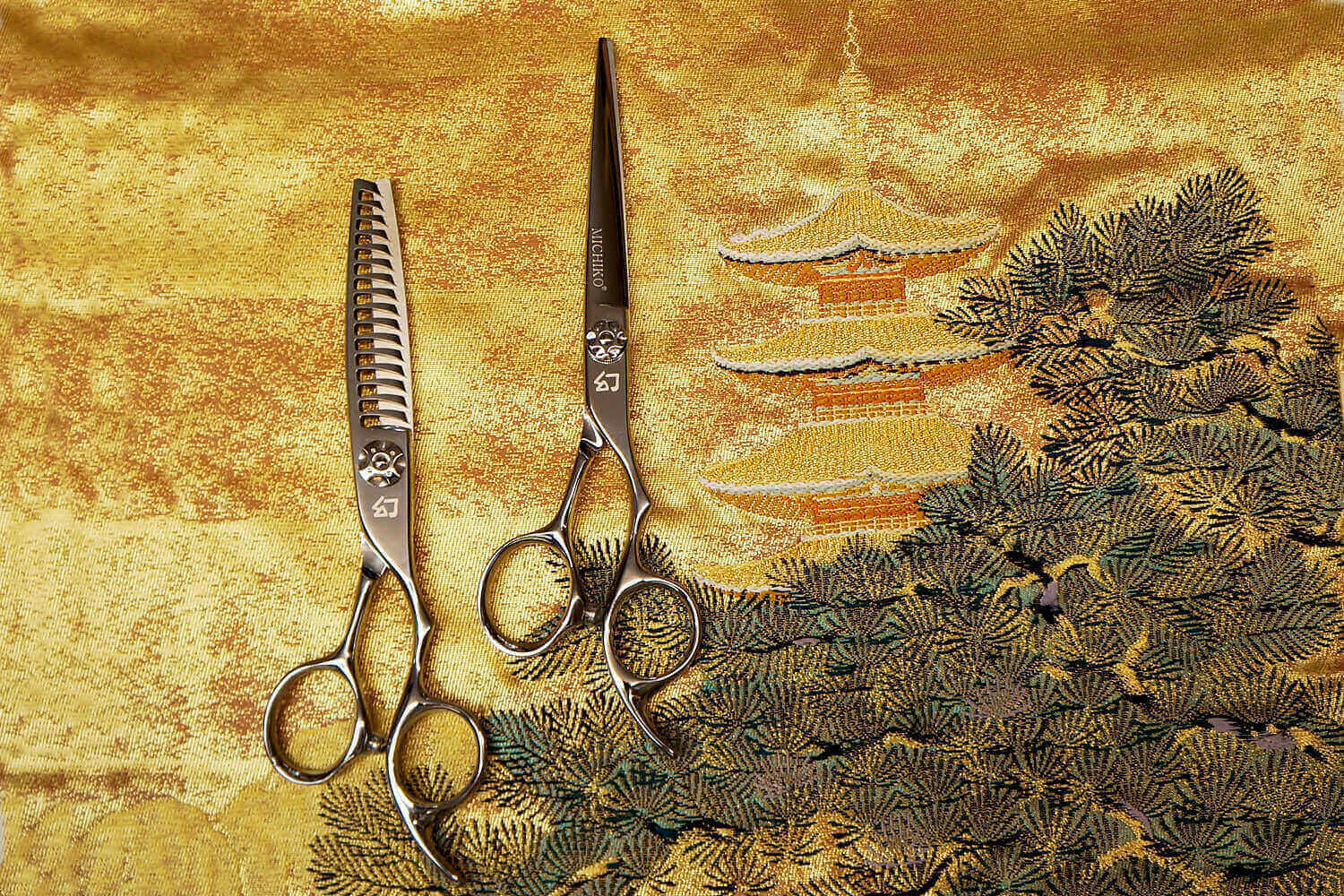 Two pair of hair cutting scissors on a golden Japanese fabric.