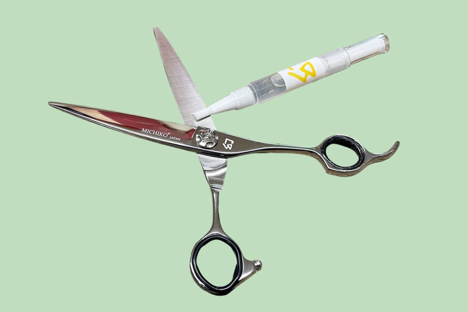 Japanese Michiko hair cutting shears being oiled for maintenance with a precision applicator on a green background.