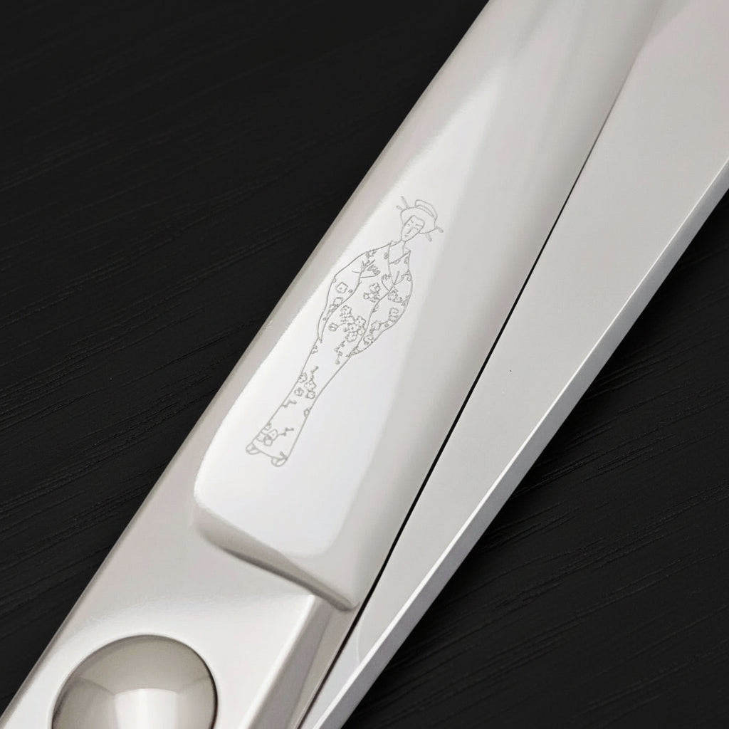 Close-up of a silver hair scissor blade with an engraved Japanes lady wearing a kimono design on a white background