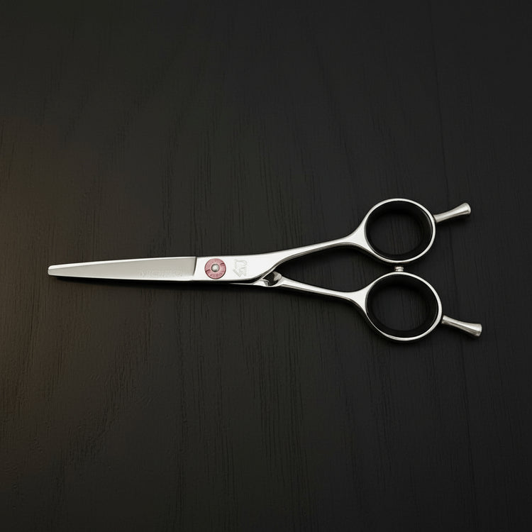 Pair of hair scissors with a pink screw on a black oak textured surface