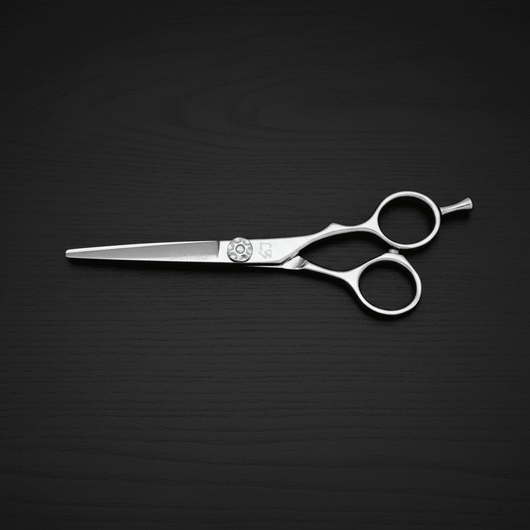 A pair of polished silver metal hair shears with a circular floral emblem in the center, resting on a dark, textured wooden surface.
