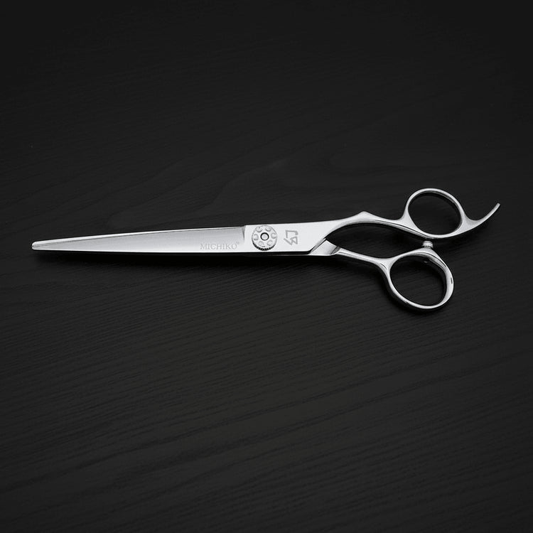 A pair of polished stainless steel professional hair shears with ergonomic loop handles, displayed diagonally on a dark wood-textured background.