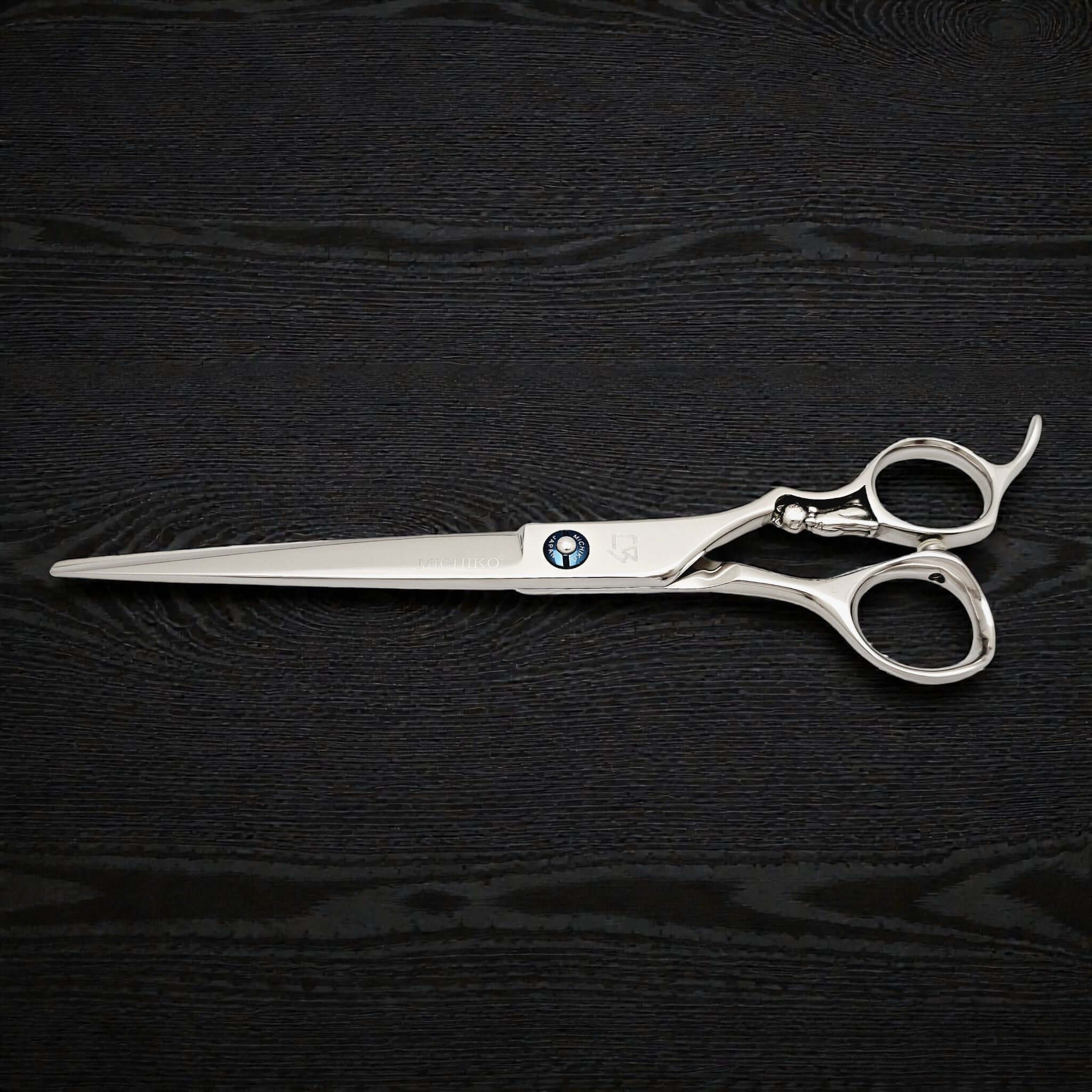 Silver scissors with a brand logo on a black textured background