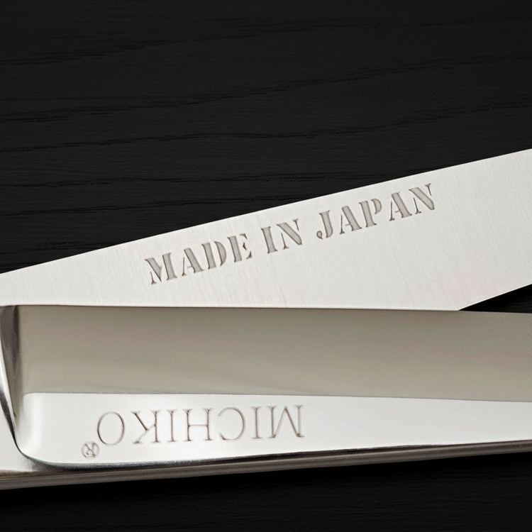 A pair of hair scissors with 'MADE IN JAPAN' and 'MICHIKO' branding on a black oak textured background