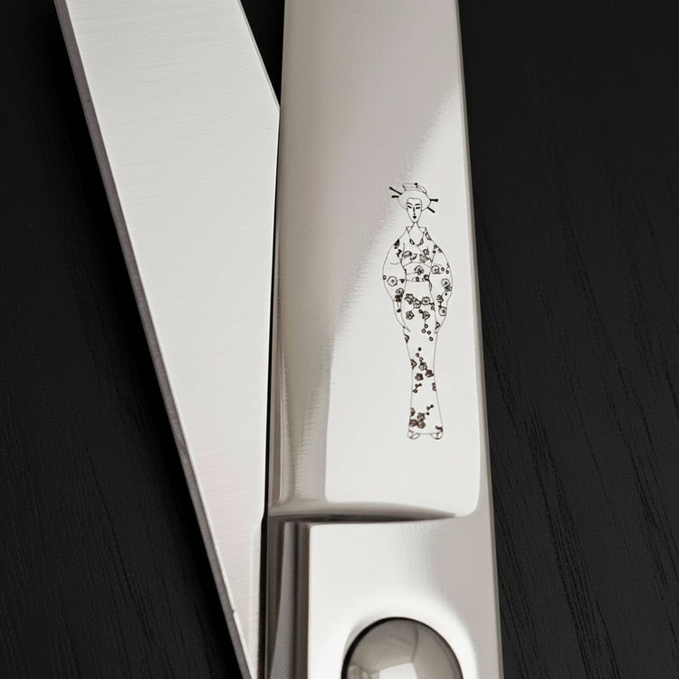 Close-up of hair scissors blades with a decorative Japanese lady wearing a kimono engraving on a black oak textured background