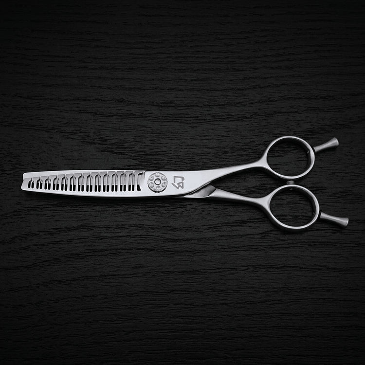 Silver hair texturizing shears with a comb-like cutting edge, shown horizontally on a dark textured background.