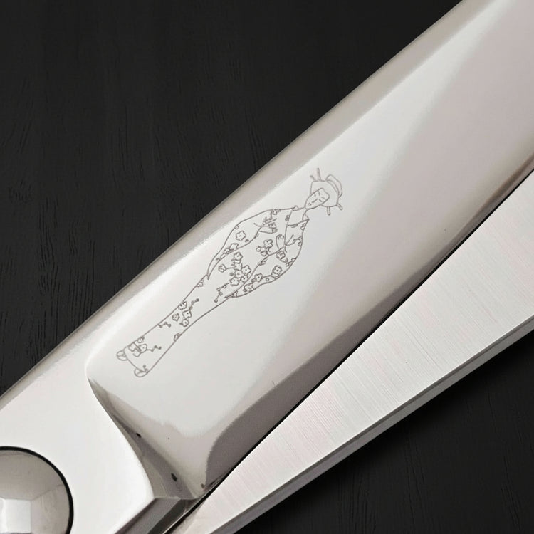 Close-up of a pair of hair scissors blades with an engraved Japanese lady wearing a kimono design on a black background