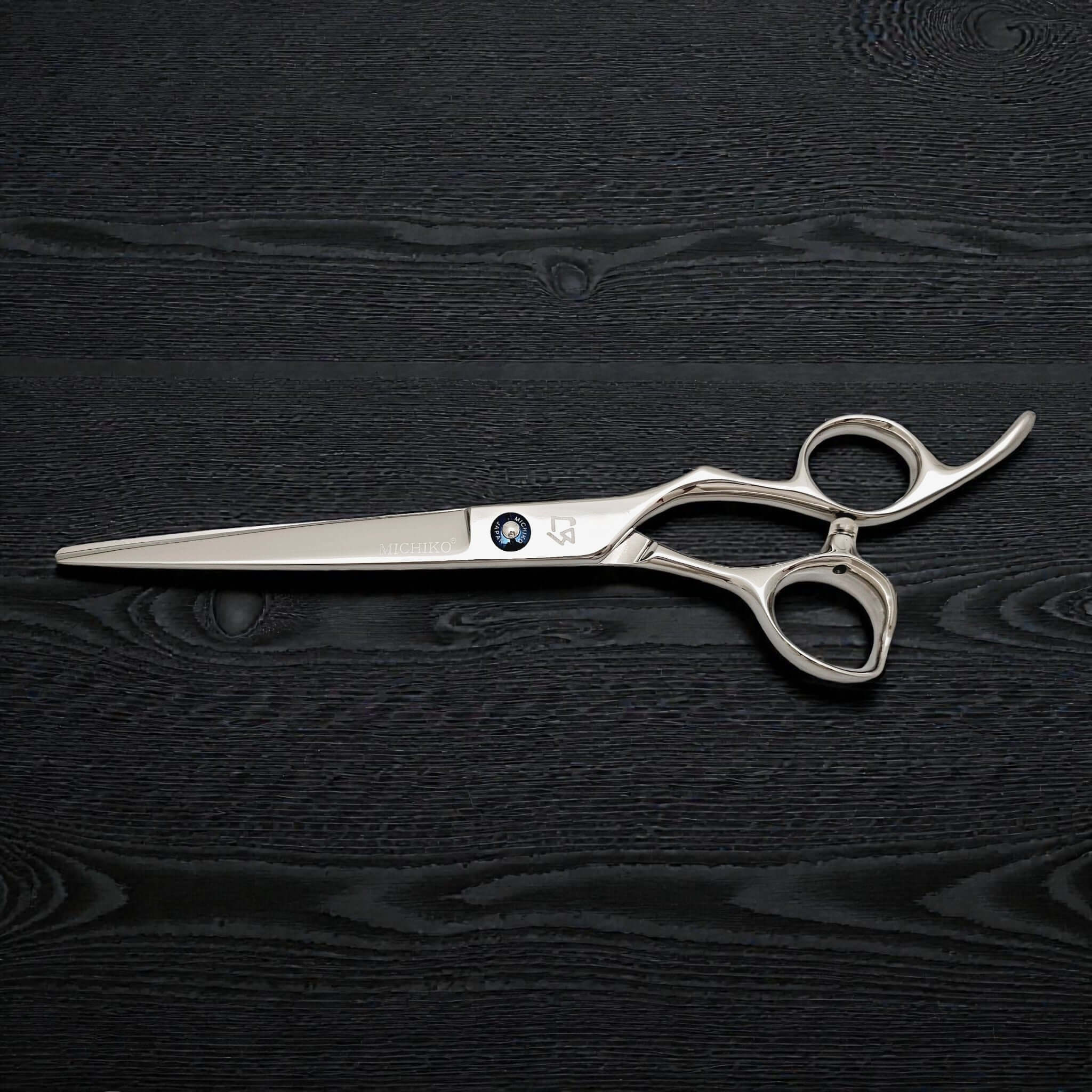 Silver scissors with a brand logo on a black wooden surface
