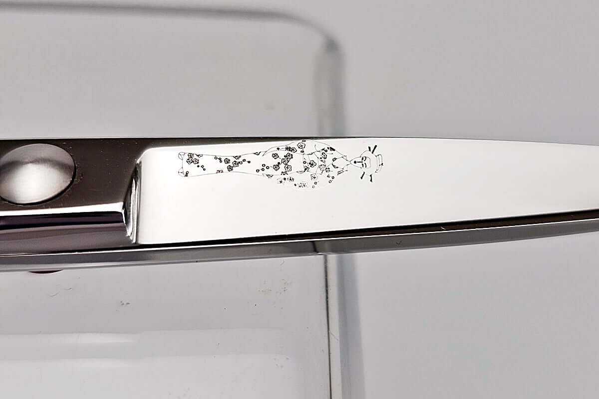 Close-up of a hair-cutting scissors blade with a MICHIKO lady logo engraved on a white background