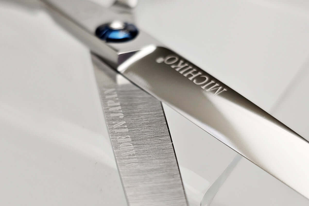 Close-up of a pair of hair scissors with 'MICHIKO' branding on a light gray background.