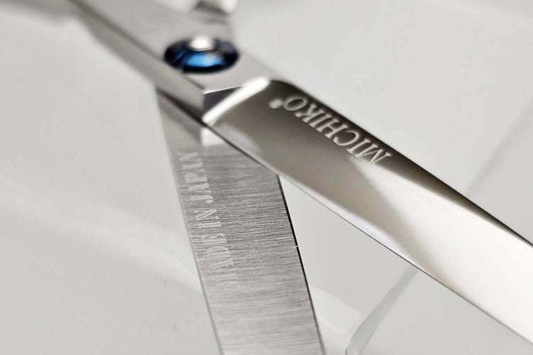 Close-up of a pair of hair scissors with 'MICHIKO' branding on a light gray background.
