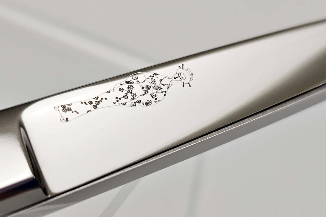 Close-up of a hair scissors blade with a MICHIKO lady logo etching on a light gray background