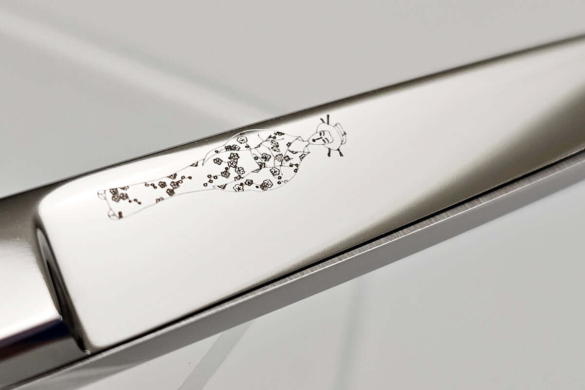 Close-up of a hair scissors blade with a MICHIKO lady logo etching on a light gray background