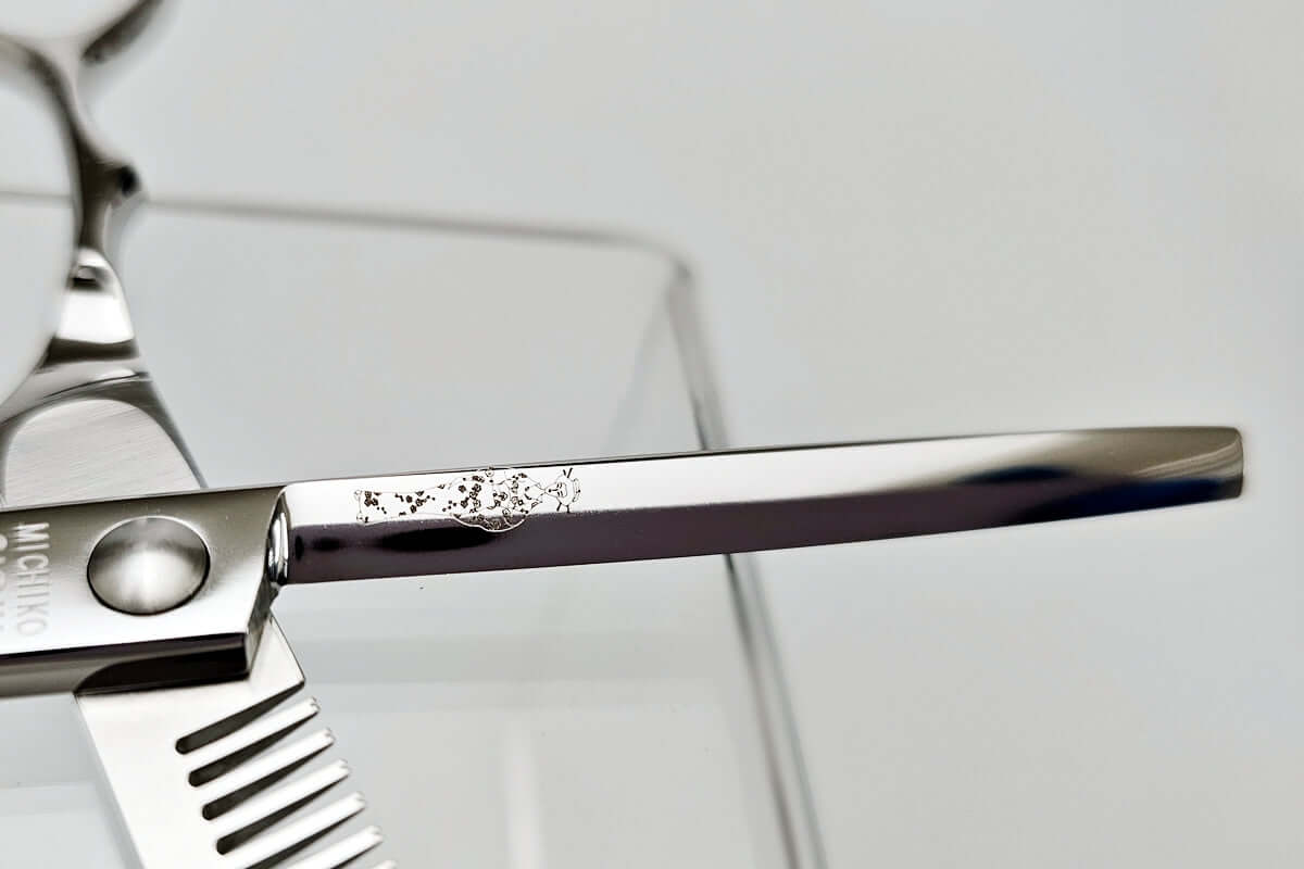 Close-up of a hair scissors blade with a MICHIKO lady logo engraved on a white background
