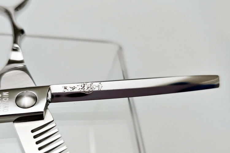 Close-up of a hair scissors blade with a MICHIKO lady logo engraved on a white background