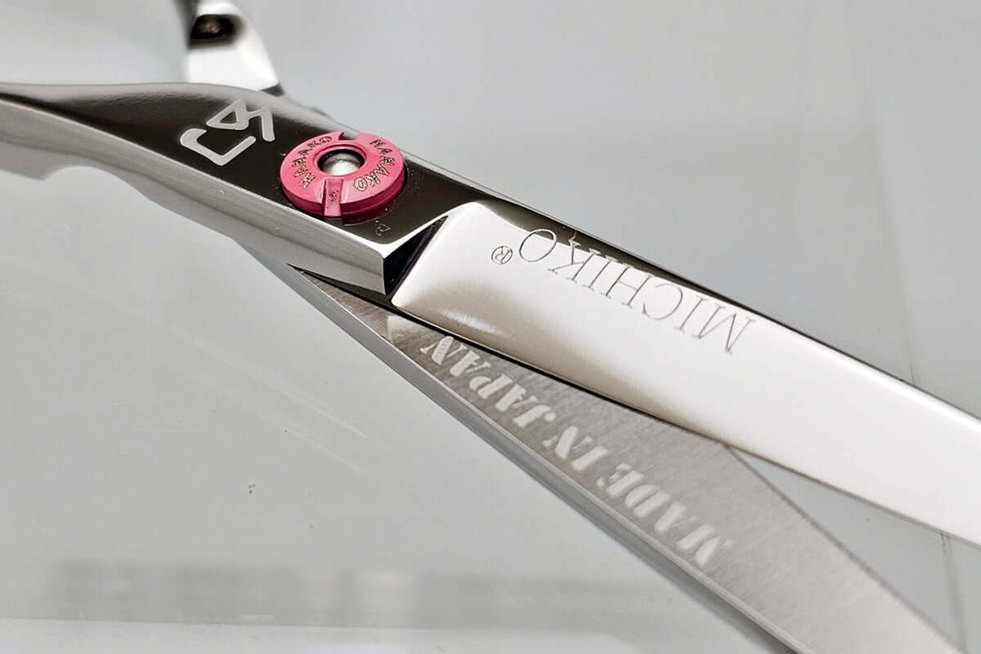 Close-up of a pair of hair scissors with 'Michiko' branding on a light gray background