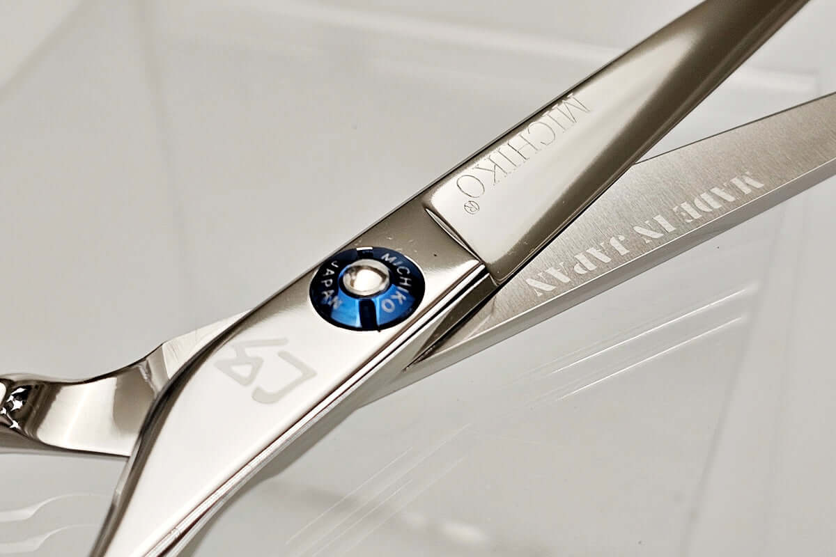 Close-up of a pair of hair scissors with brand logos on a light gray background