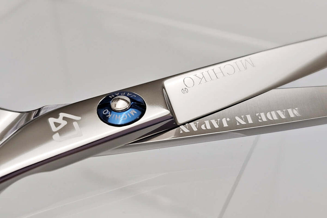 Close-up of a pair of hair scissors with 'Michiko' branding on a light gray background