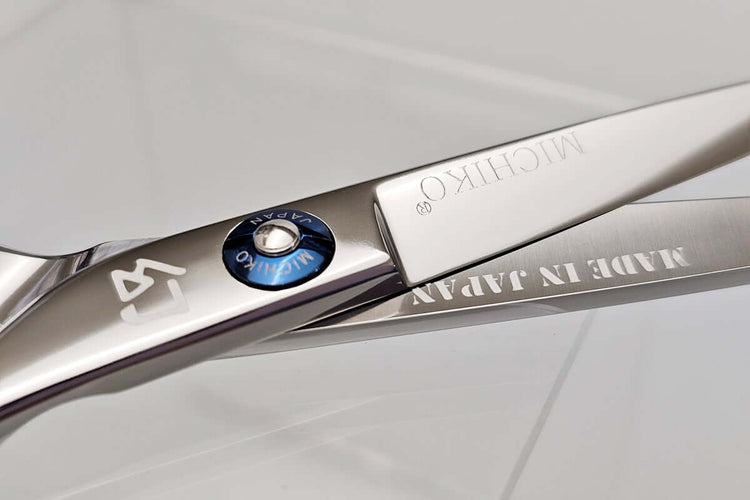 Close-up of a pair of hair scissors with 'Michiko' branding on a light gray background