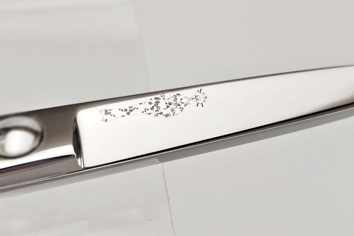 Close-up of a hair scissors blade with the MICHIKO lady logo engraved on a white background