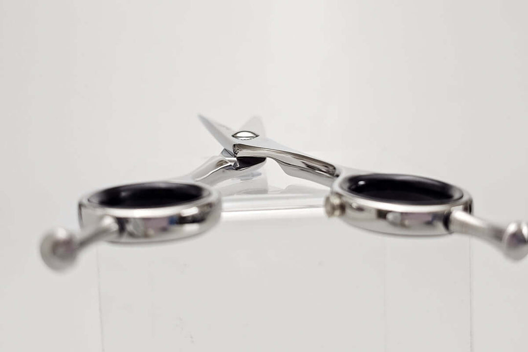Pair of silver hair scissors with black handles on a white background