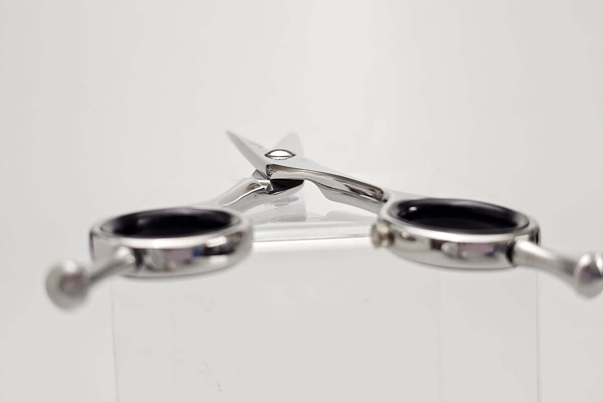 Pair of silver hair scissors with black handles on a white background