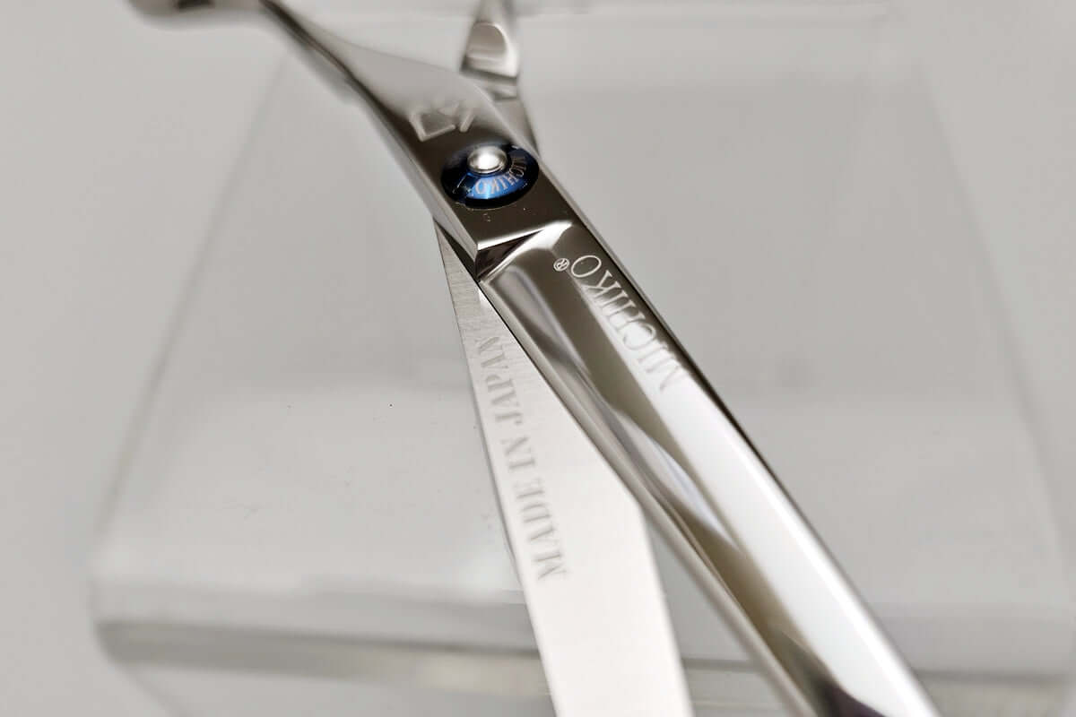 Close-up of a pair of scissors with a brand name on a light gray background