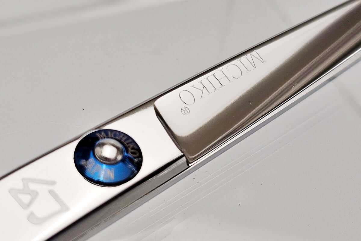 Close-up of a hair scissors with 'Michiko' branding on a gray background