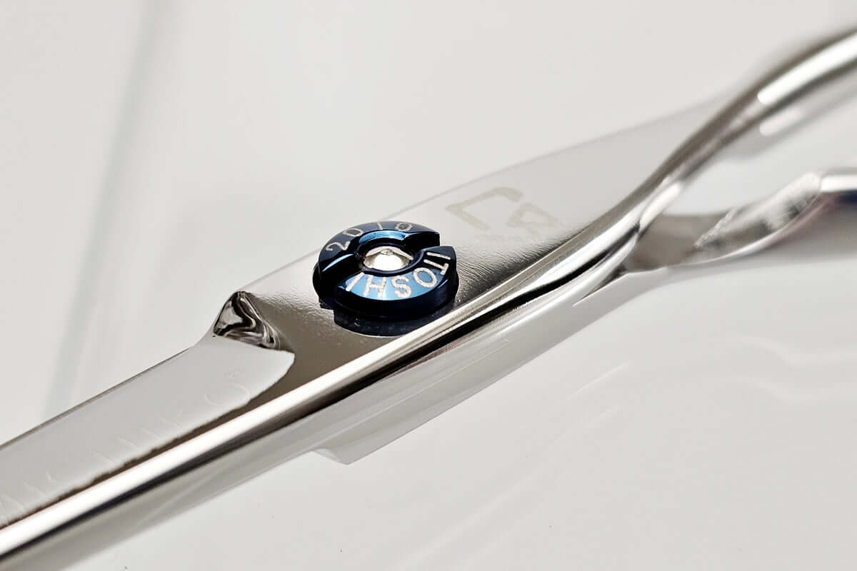 Close-up of a pair of hair scissors with a brand logo on a light gray background