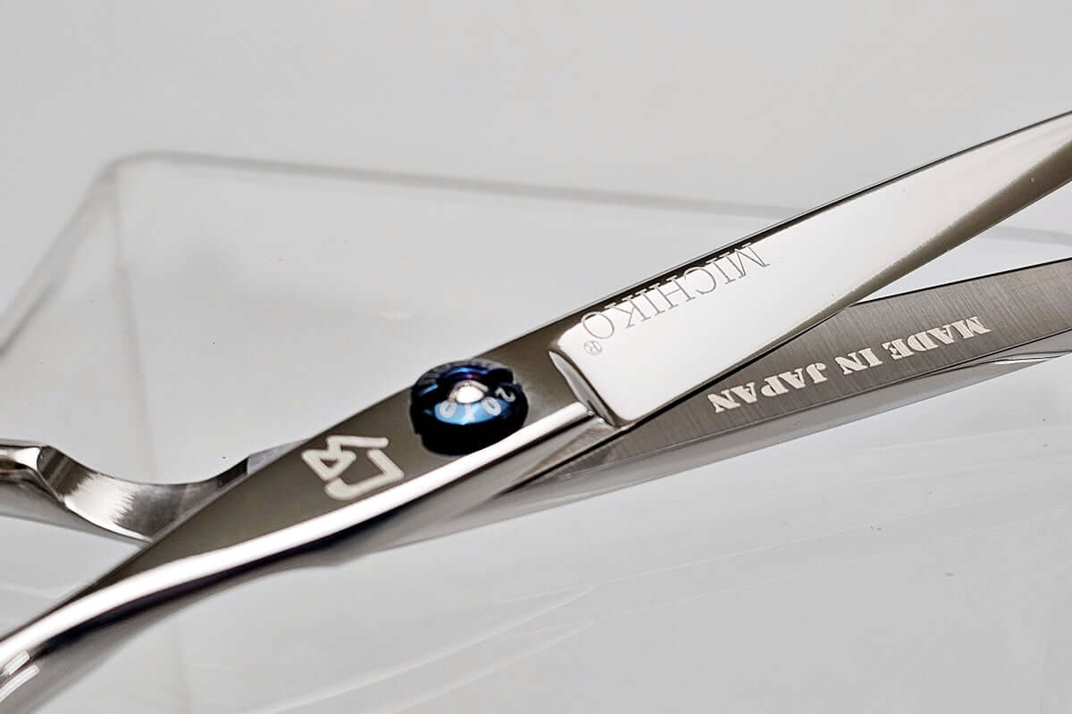 Close-up of a pair of hair scissors with 'Michiko' branding on a light gray background