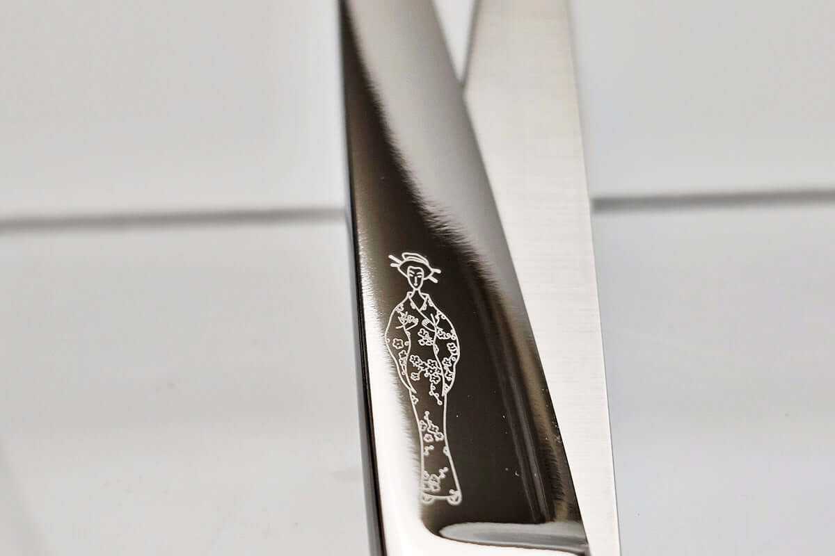Close-up of a hair scissor blade with a Michiko lady logo engraved on a light gray background